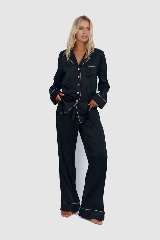 Woman wearing a black pajama set with white piping on a white background